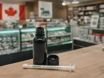Black 30 mL plastic bottle with cap and oral dosing syringe displayed on a counter in a Canadian cannabis retail store setting